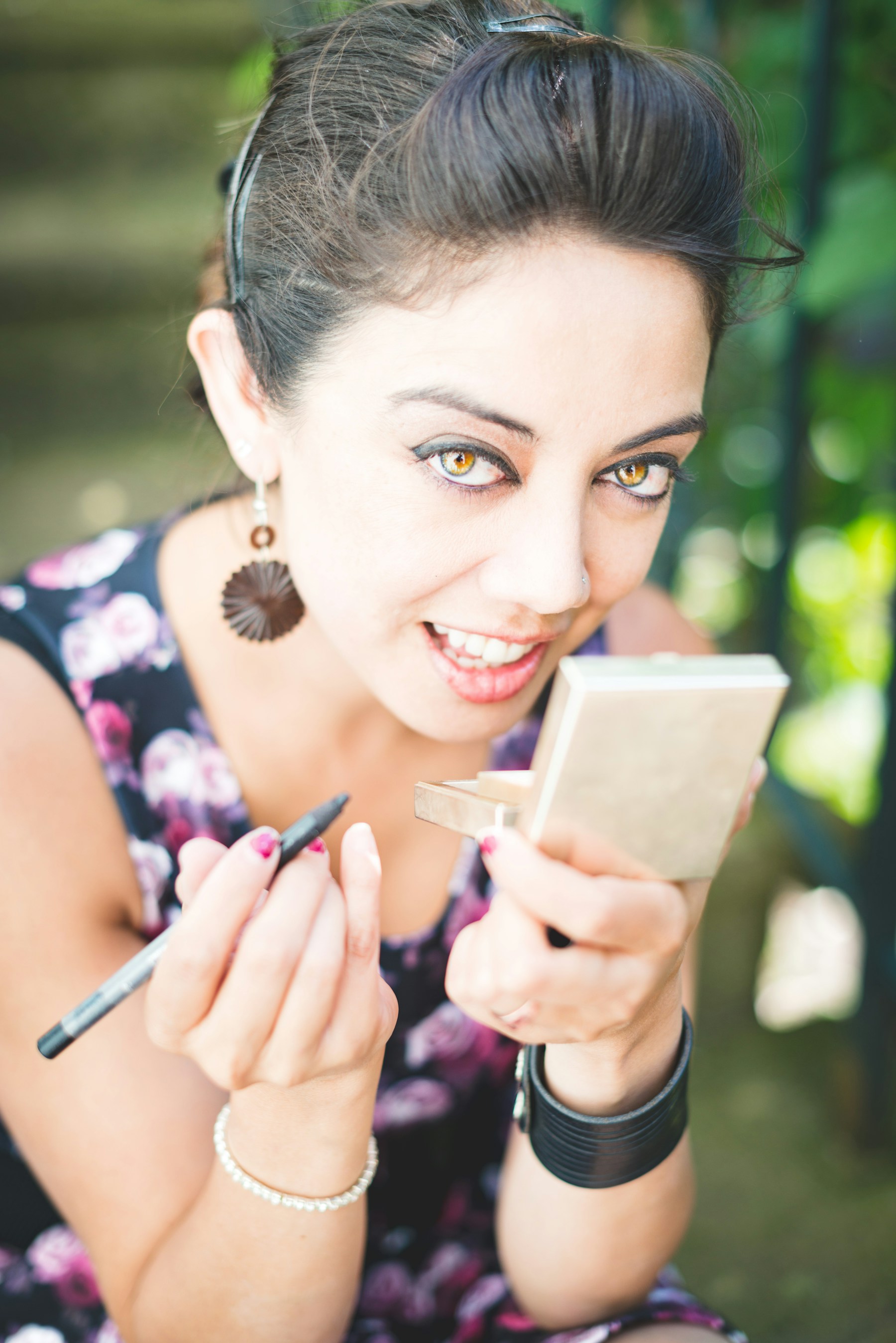 smiling woman holding mirror and pencil eyeliner